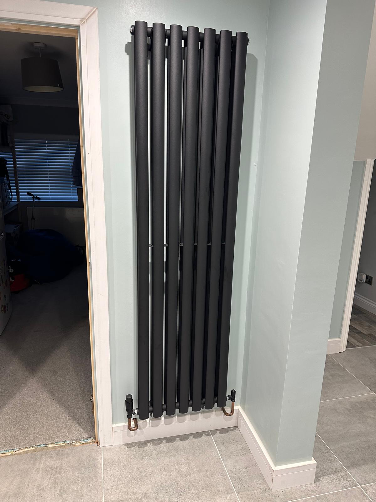 Anthracite vertical column radiator installed on a pale blue wall in a Northamptonshire home