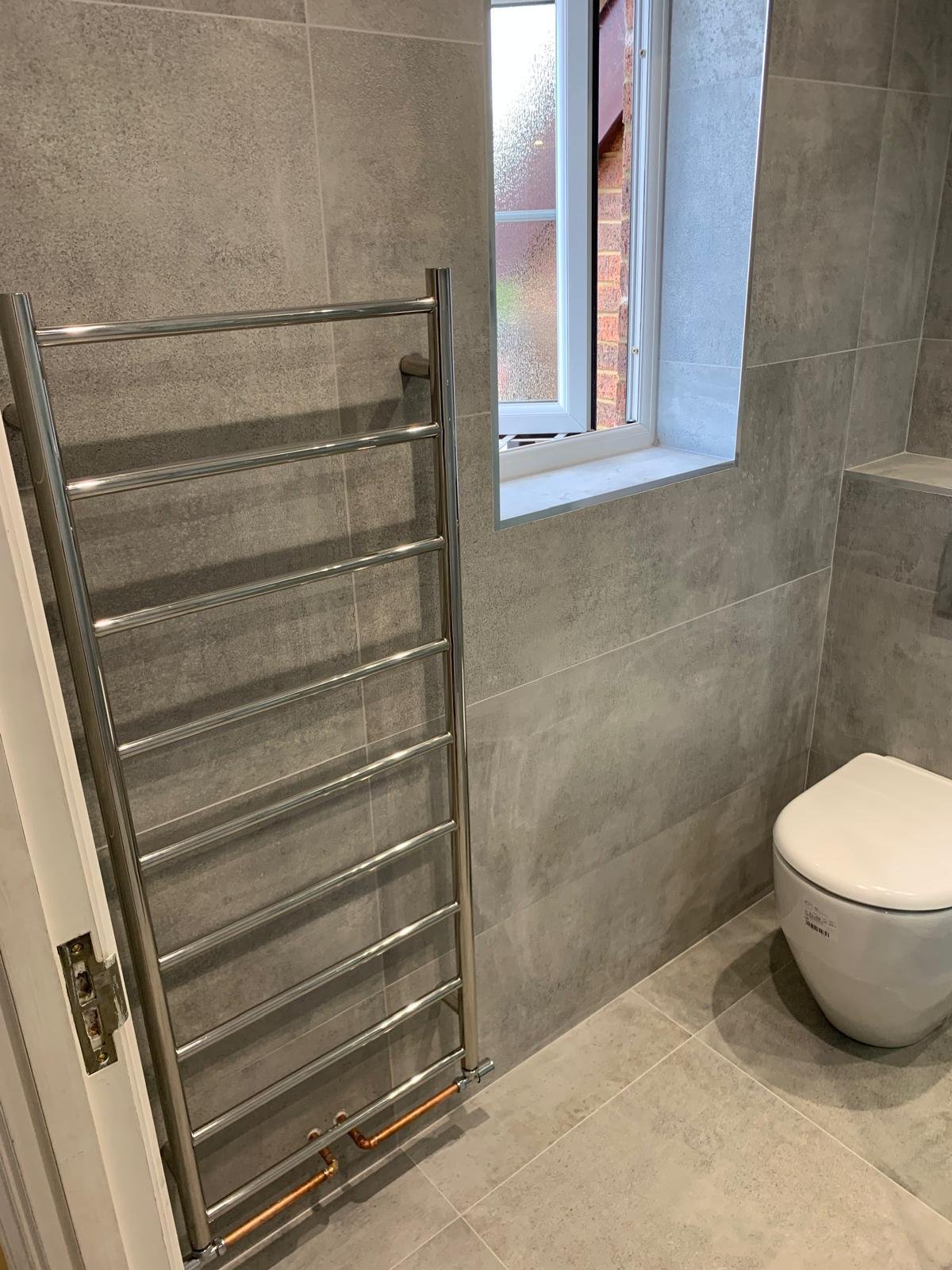Shower room with a wall hung toilet and a tall chrome towel rail