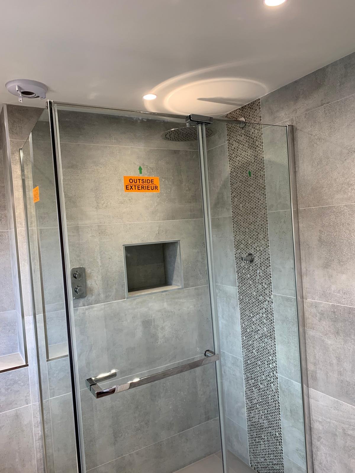 Walk in shower enclosure with a tiled niche and a mosaic feature strip
