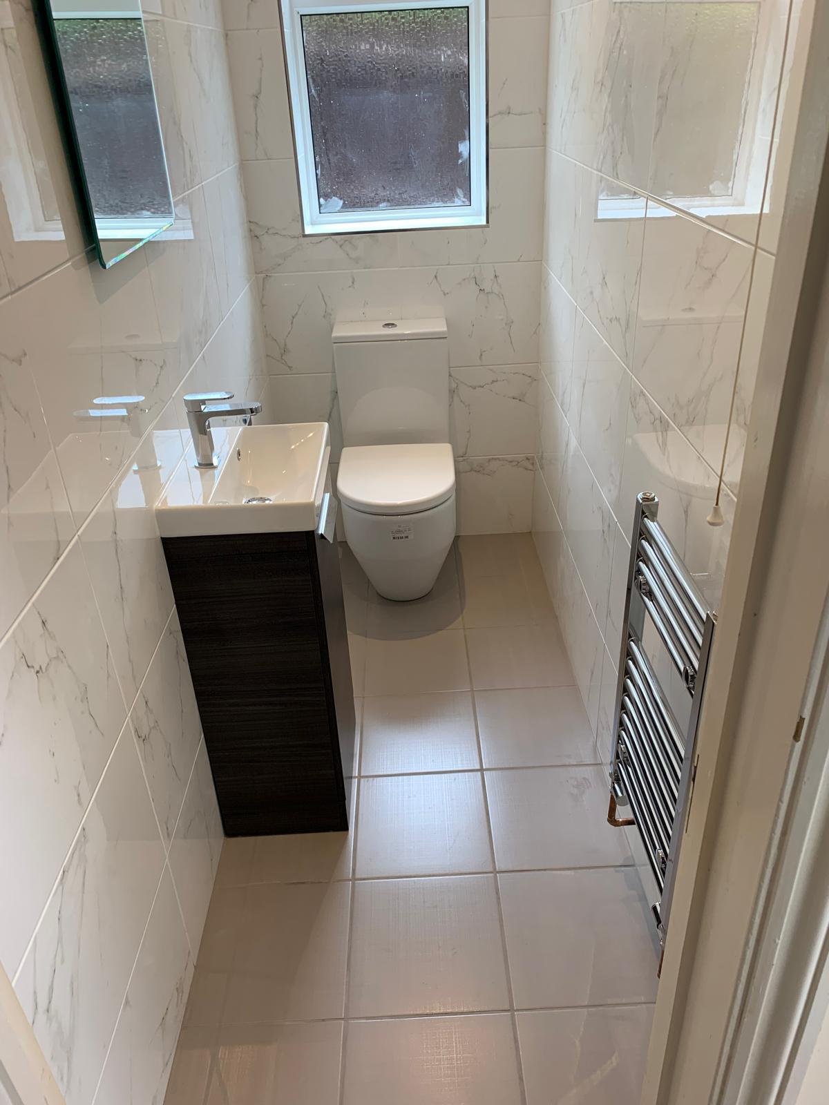 Downstairs cloakroom with marble effect tiling, a dark vanity unit and a chrome towel rail